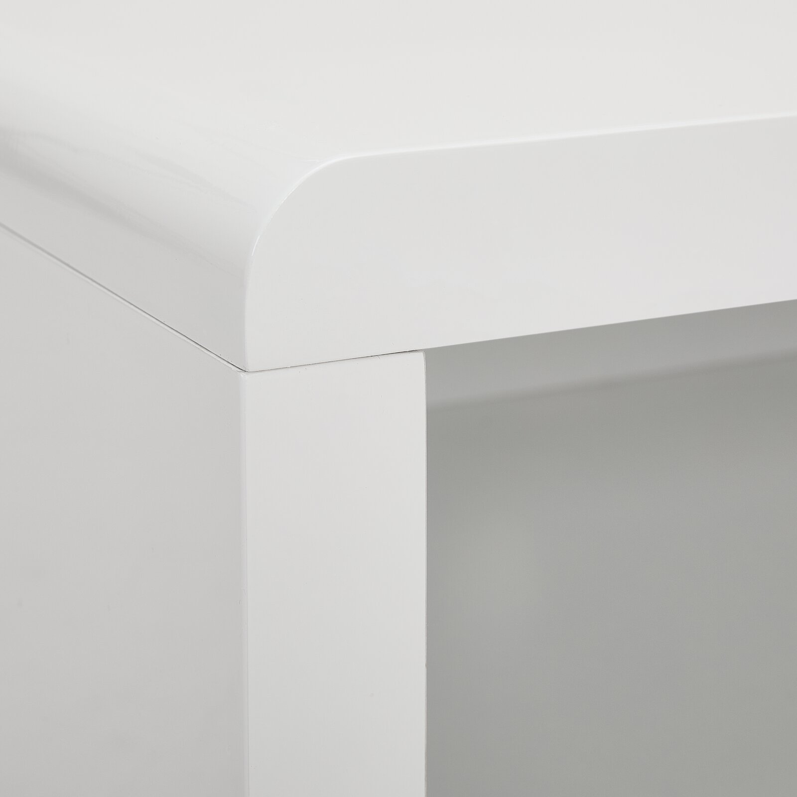 Nahaufnahme einer Ecke eines weißen TV-Lowboards mit abgerundeten Kanten, Perspektive von oben.