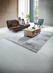 Moderner Couchtisch aus Holz mit Regalfächern, frontal im Wohnzimmer platziert, umgeben von einem Sofa, einem Sessel und einem Teppich.