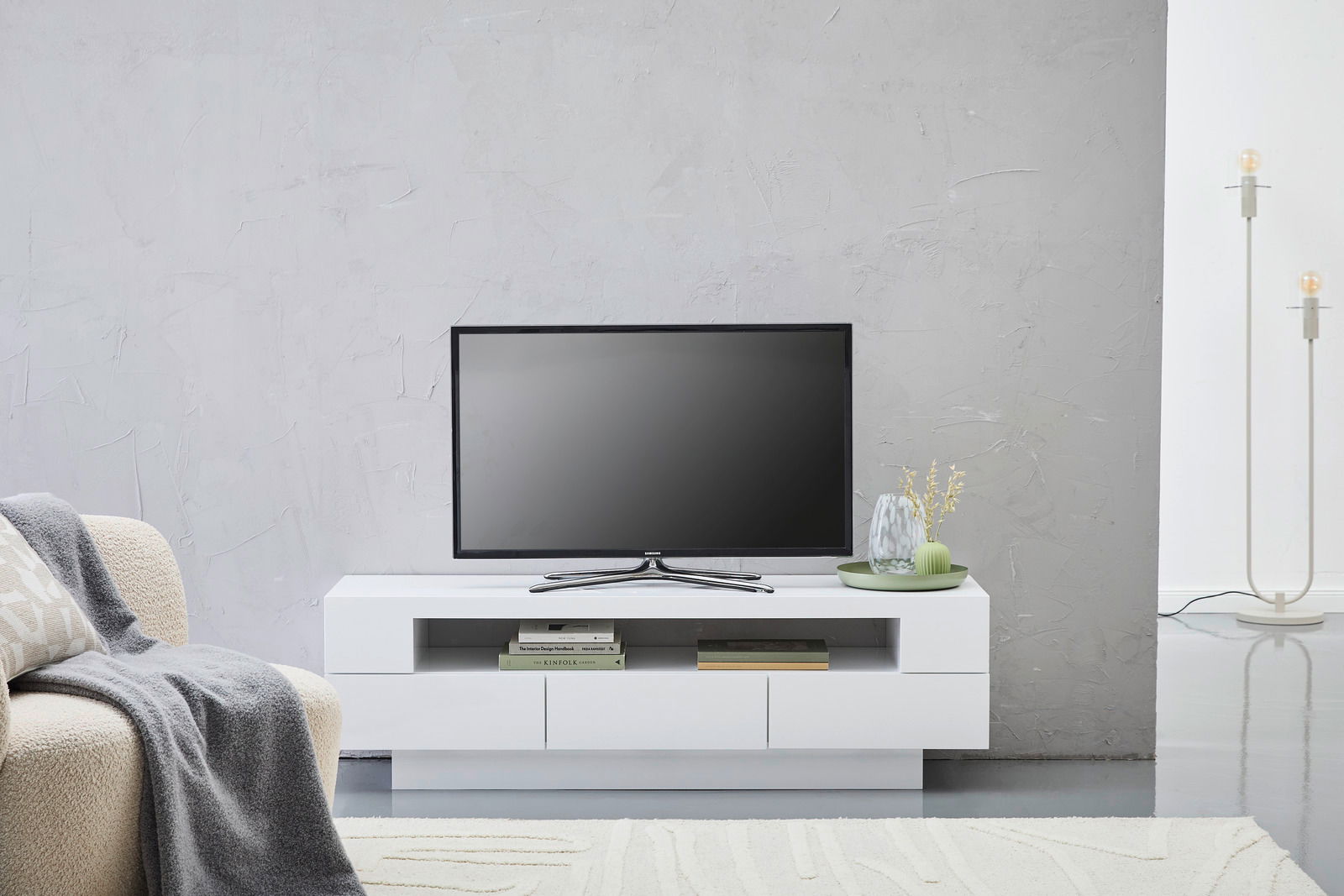 Modernes weißes Lowboard mit Fernseher, dekoriert mit Büchern und Vasen, aus frontaler Perspektive.