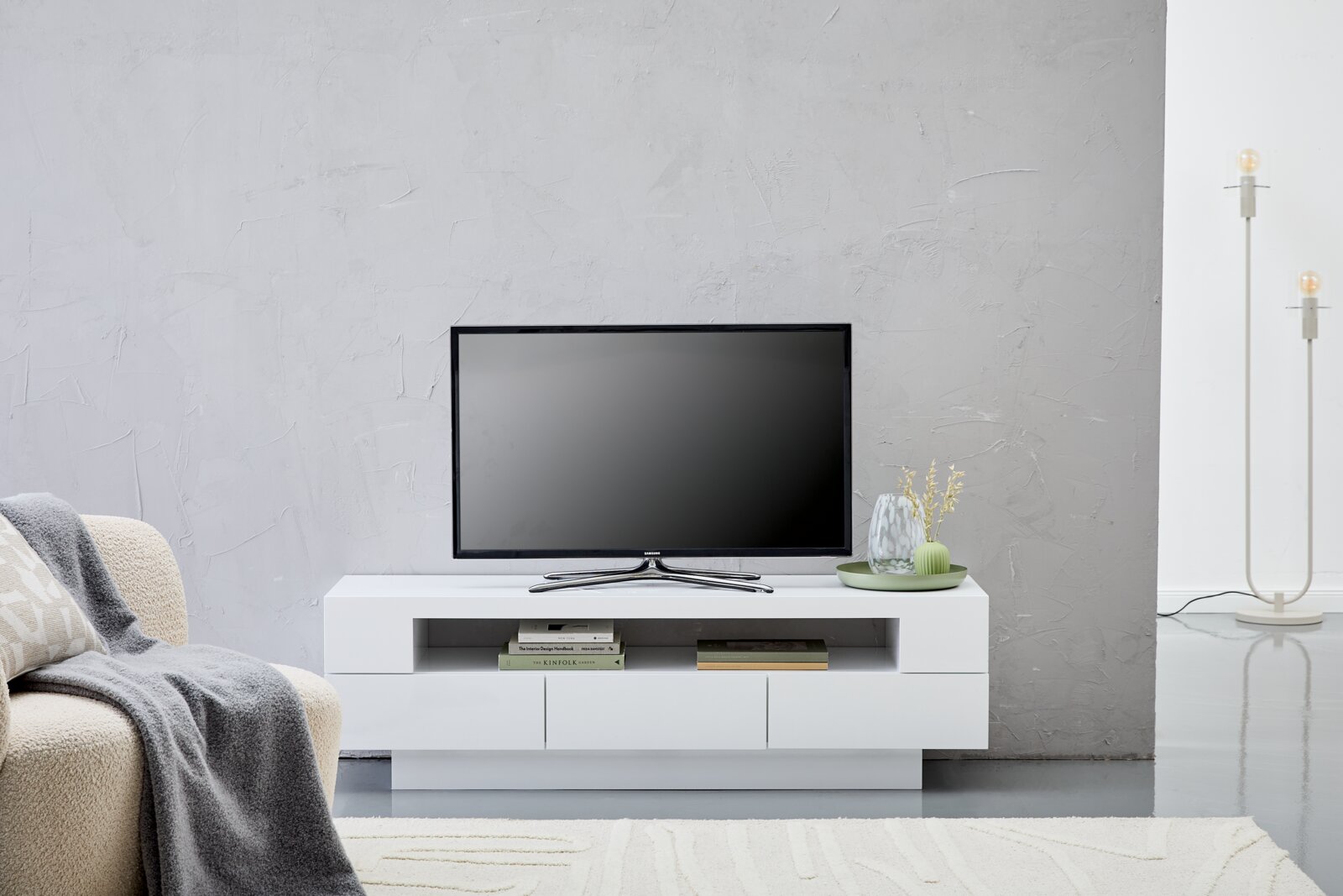 Modernes weißes Lowboard mit Fernseher, dekoriert mit Büchern und Vasen, aus frontaler Perspektive.