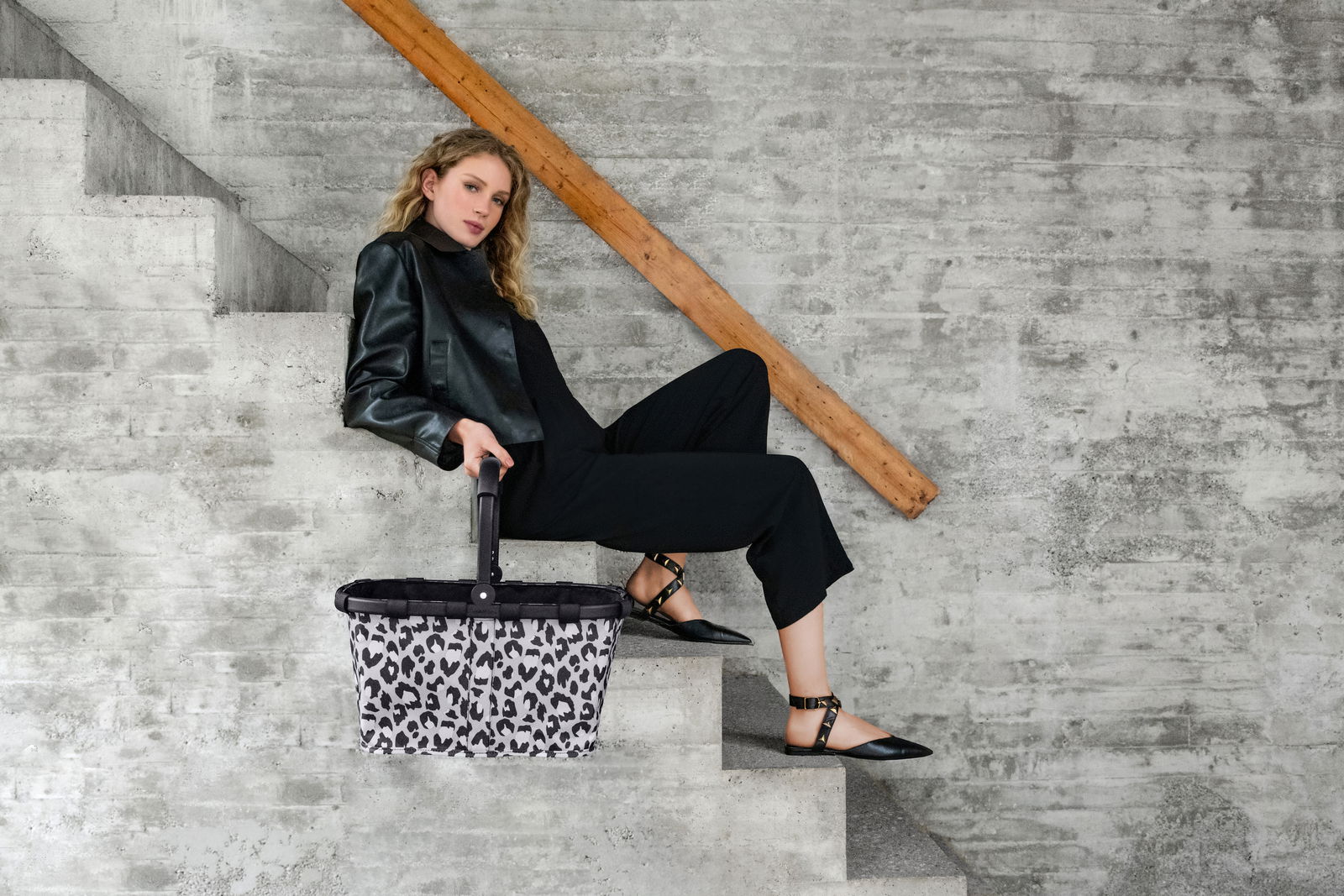 Frau sitzt auf einer Treppe und hält einen Einkaufskorb mit Leopardenmuster in der Hand, seitliche Perspektive.