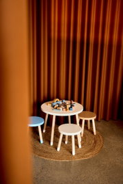 Kindertisch und Hocker-Set in einem gemütlichen Raum mit Vorhängen im Hintergrund, aus der Perspektive von schräg oben fotografiert.