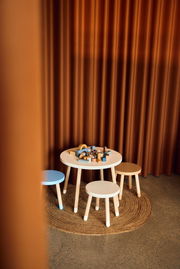 Kindertisch und Hocker-Set in einem gemütlichen Raum mit Vorhängen im Hintergrund, aus der Perspektive von schräg oben fotografiert.