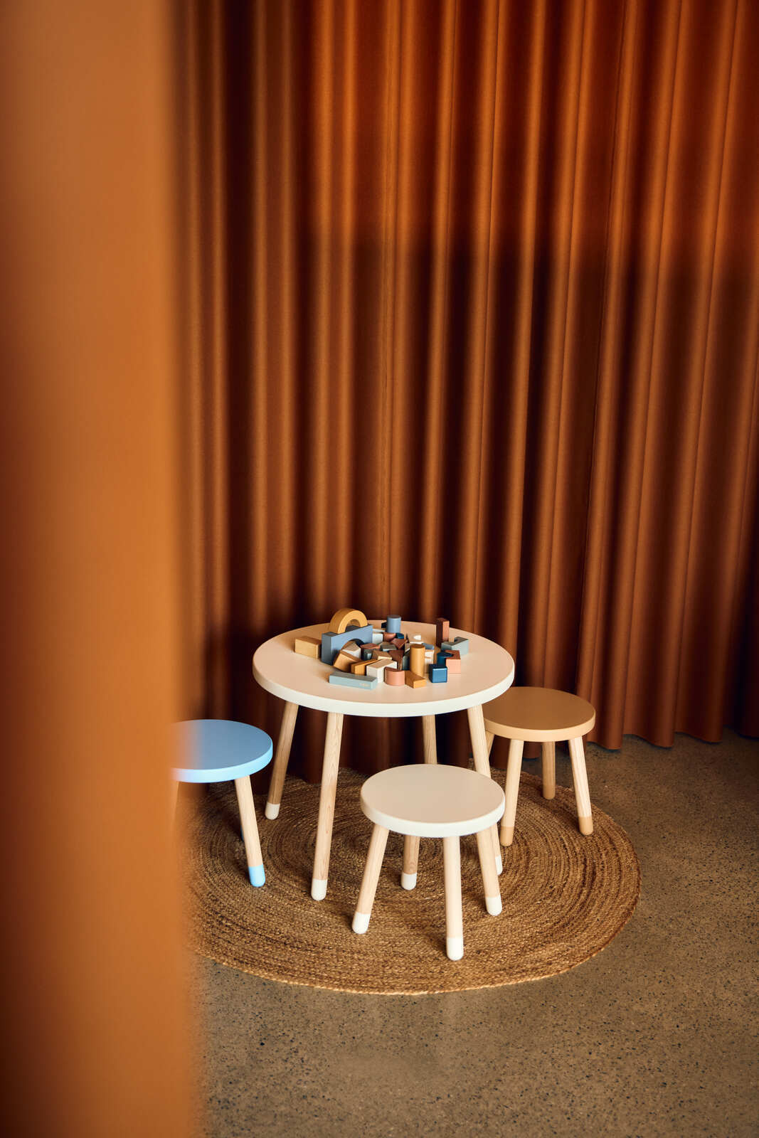 Kindertisch und Hocker-Set in einem gemütlichen Raum mit Vorhängen im Hintergrund, aus der Perspektive von schräg oben fotografiert.
