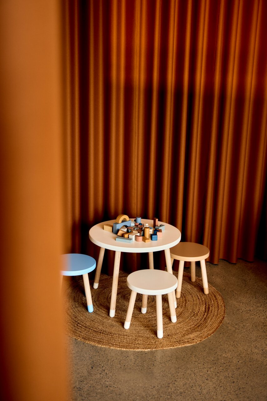 Kindertisch und Hocker-Set in einem gemütlichen Raum mit Vorhängen im Hintergrund, aus der Perspektive von schräg oben fotografiert.