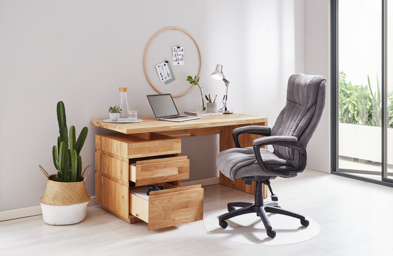 Moderner Chefsessel in Grau vor einem Holzschreibtisch mit geöffneter Schublade, seitliche Perspektive