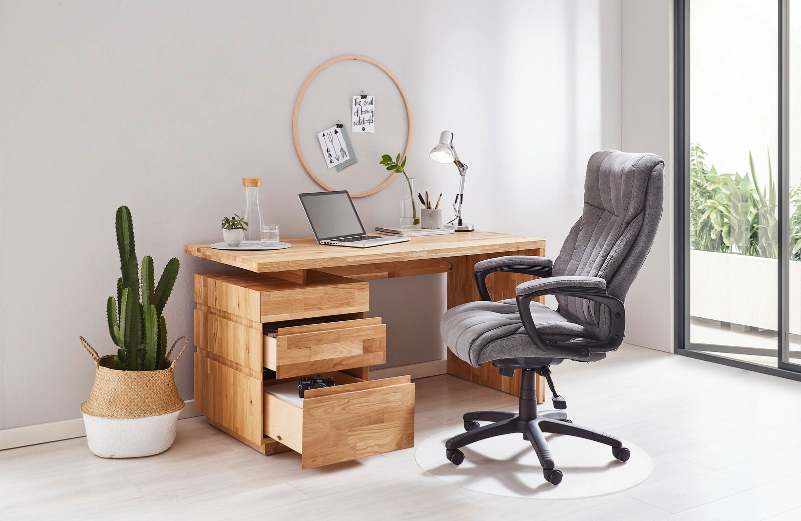 Moderner Chefsessel in Grau vor einem Holzschreibtisch mit geöffneter Schublade, seitliche Perspektive