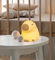 Niedliches Akku-Nachtlicht in Form eines leuchtenden gelben Schweinchens, frontal auf einem Tisch in einem Kinderzimmer platziert.