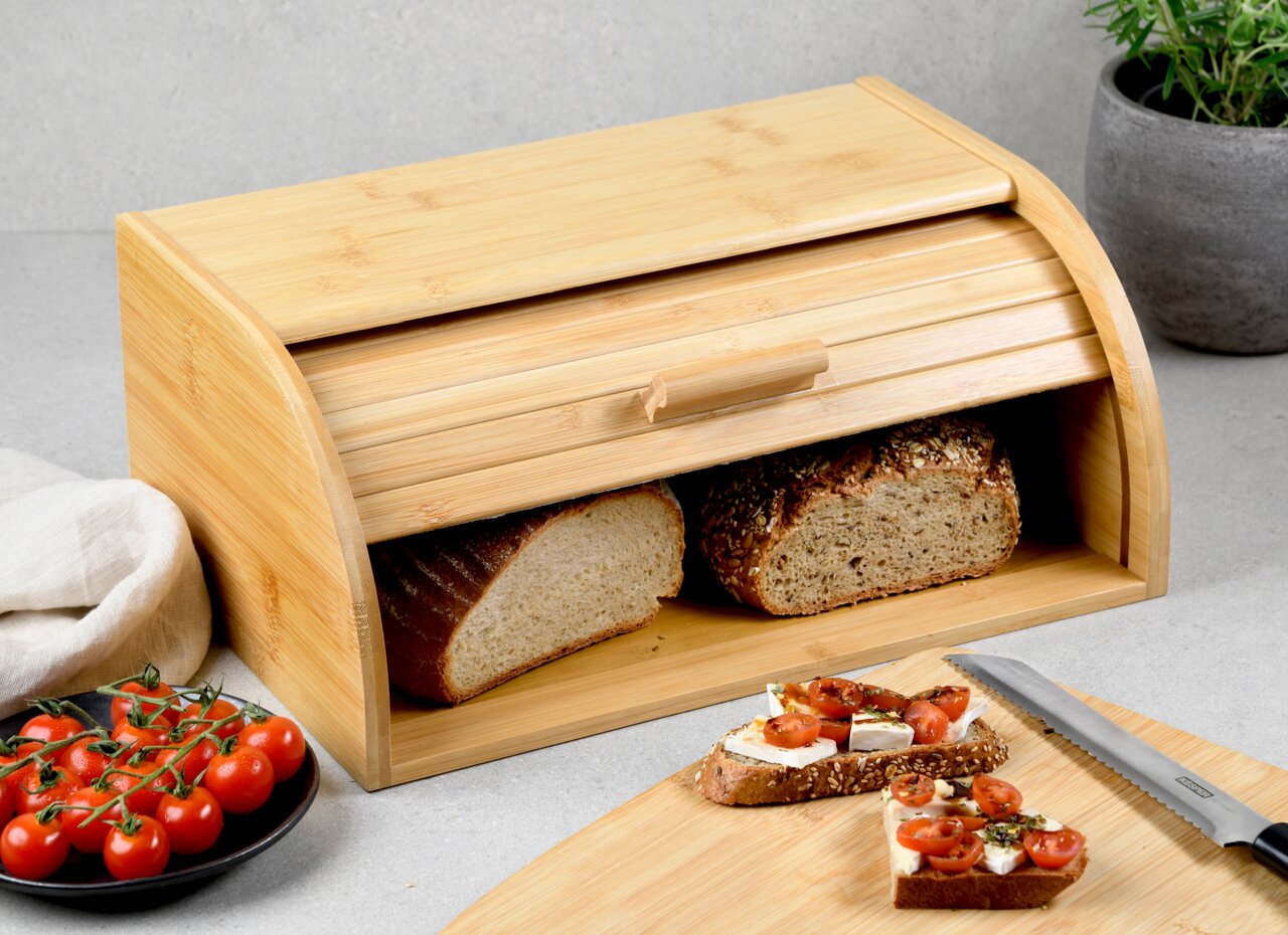 Bambus-Brotkasten mit Rollklappe, gefüllt mit Brotscheiben, auf einer Küchenarbeitsplatte. Perspektive von vorne.