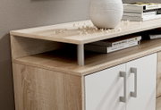 Nahaufnahme eines modernen Sideboards mit Holzoptik und weißen Türen, dekoriert mit Büchern und einer Vase, aus seitlicher Perspektive.