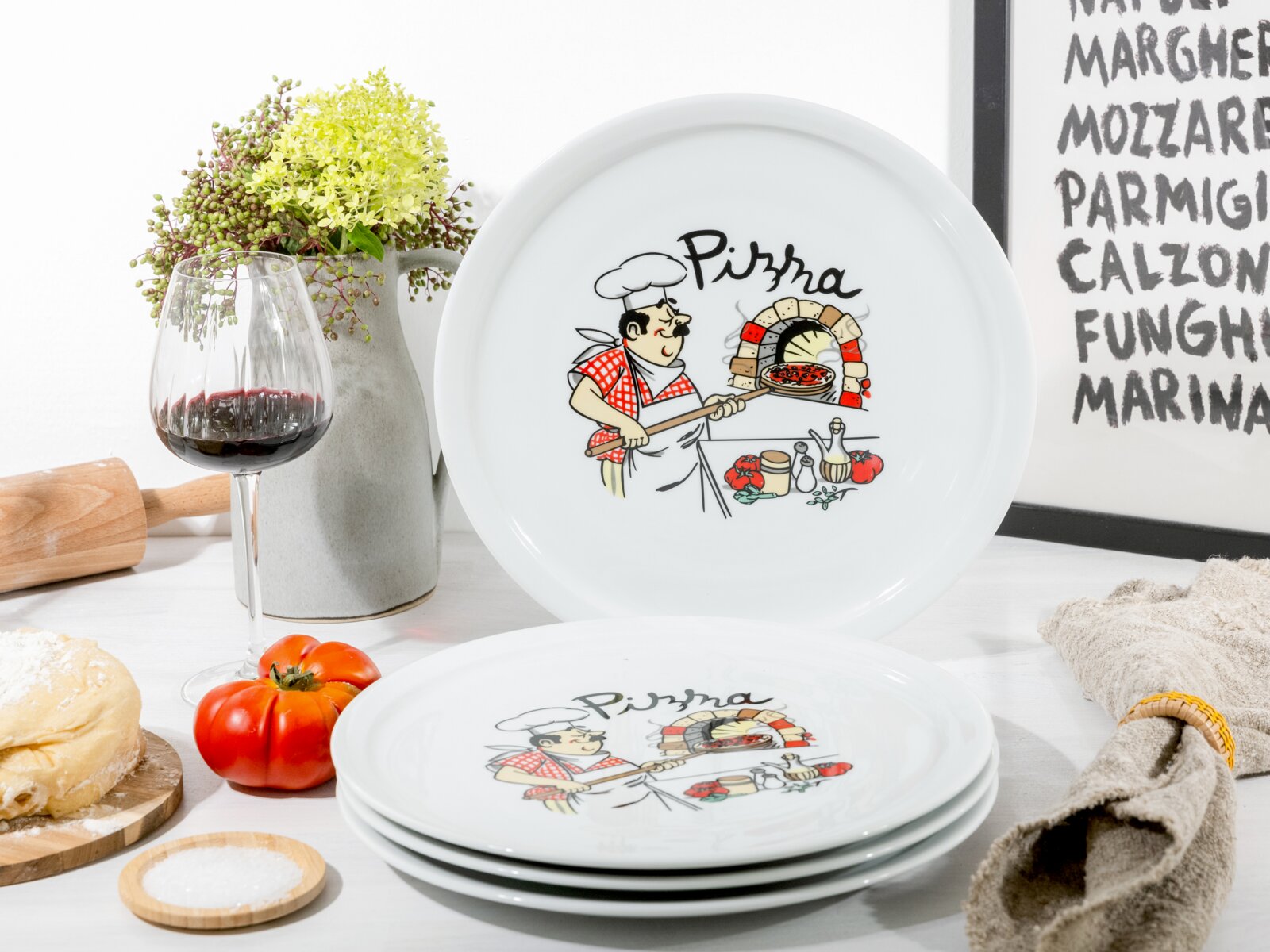creaTable Pizzateller 4-tlg MILANO Weiße Pizza-Teller mit Comic-Motiv eines Pizzabäckers am Steinofen und Schriftzug „Pizza“, aufgedeckter Teller frontal im Hintergrund und gestapelte Teller in leicht schräger Perspektive im Vordergrund, arrangiert mit Rotweinglas, Tomaten, Brot und Vase a