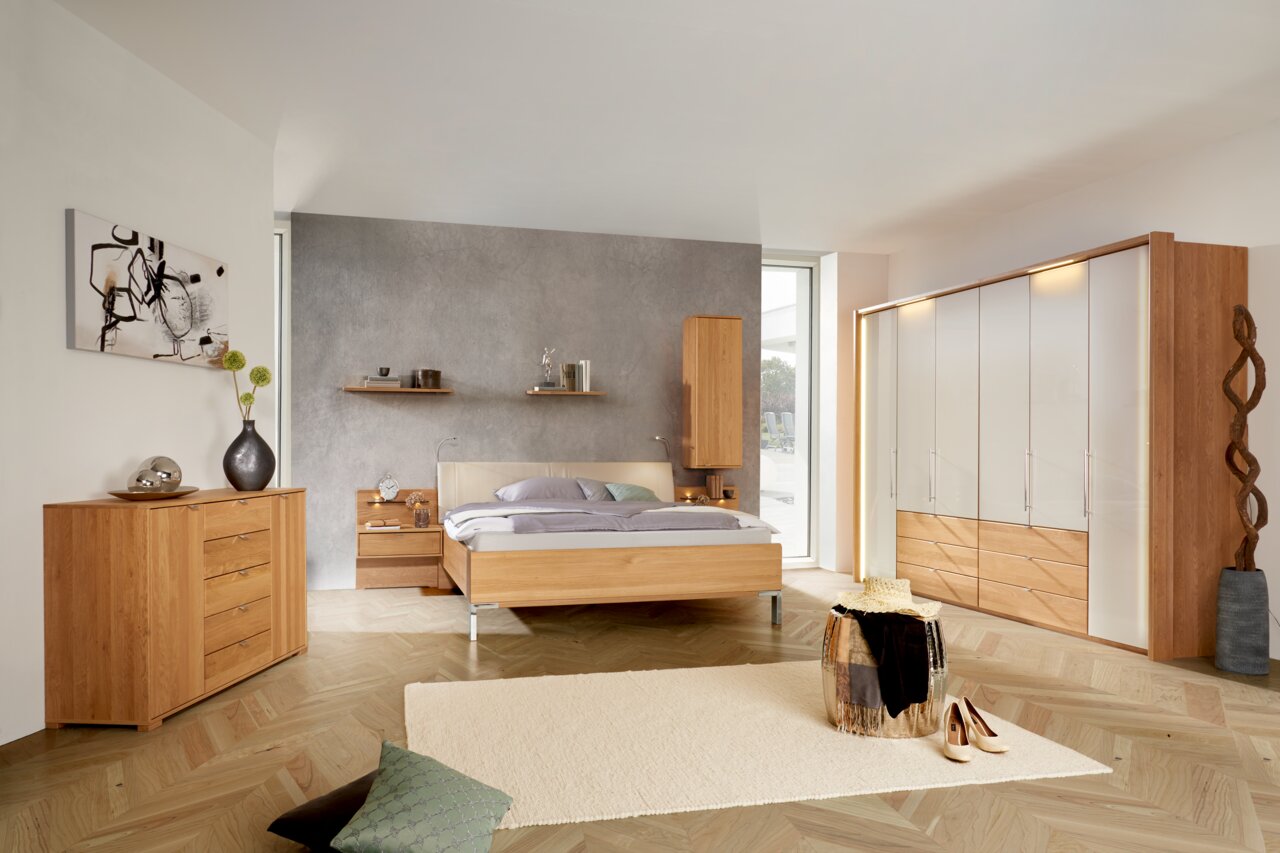 Schlafzimmer mit modernem Dieter Knoll Gleittürenschrank AMATO in Holzoptik und weißen Fronten, seitliche Perspektive.