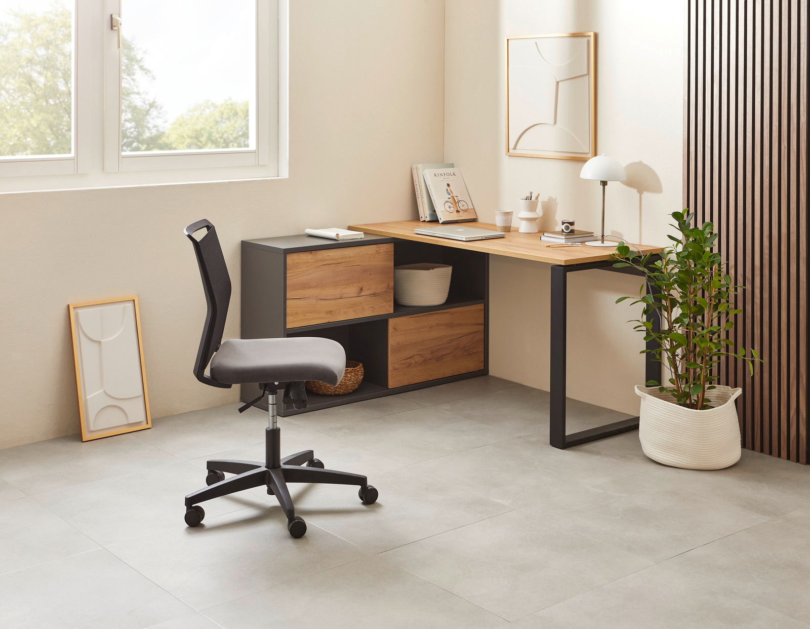 Moderner Winkelschreibtisch in einem hellen Raum, mit einem schwarzen Metallrahmen und Holzoberfläche, seitlich von einem Fenster beleuchtet. Ein ergonomischer Bürostuhl steht davor, und eine Pflanze in einem weißen Korb ergänzt das minimalistische Design
