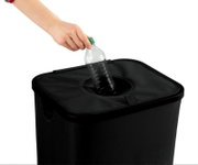 Een hand gooit een plastic fles in een zwarte statiegeldcontainer. Aanzicht van bovenaf.