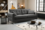 Modernes graues Stoffsofa mit Steppung, breiten Armlehnen und verchromten Füßen im Wohnzimmer, perspektivisch in leichter Frontansicht von links.