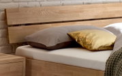 Holz-Kopfteil eines Bettes mit zwei Kissen, eines in Grau und eines in Gold, aus seitlicher Perspektive
