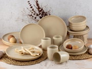 Beige Kombiservice 16-teilig, bestehend aus Tellern, Schalen und Bechern, auf einem Tisch mit natürlicher Dekoration, seitliche Perspektive