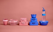 Verschillende lunchboxen en bakjes in roze en blauw, vooraanzicht op een roze achtergrond.