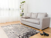 Designer Teppich in einem modernen Wohnzimmer mit grauem Sofa und Holzfußboden, aus der Perspektive von vorne links betrachtet.