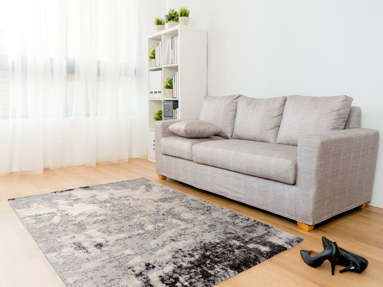 OCI Designer Teppich JUWEL Designer Teppich in einem modernen Wohnzimmer mit grauem Sofa und Holzfußboden, aus der Perspektive von vorne links betrachtet.