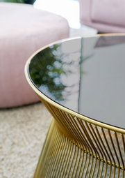 Nahaufnahme eines eleganten Couchtisches mit schwarzer Glasplatte und goldfarbenem Metallgestell, seitliche Perspektive.