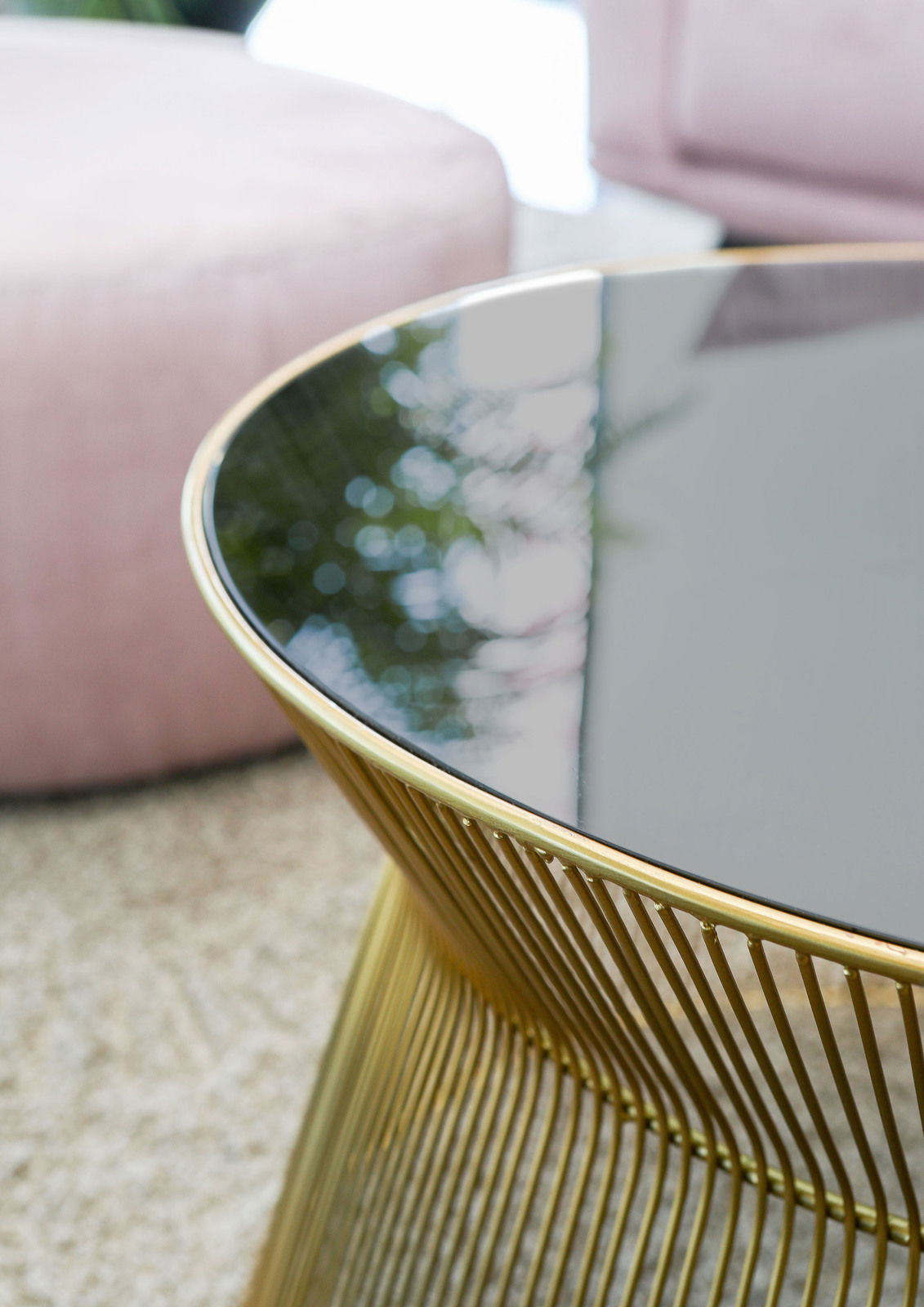 Nahaufnahme eines eleganten Couchtisches mit schwarzer Glasplatte und goldfarbenem Metallgestell, seitliche Perspektive.