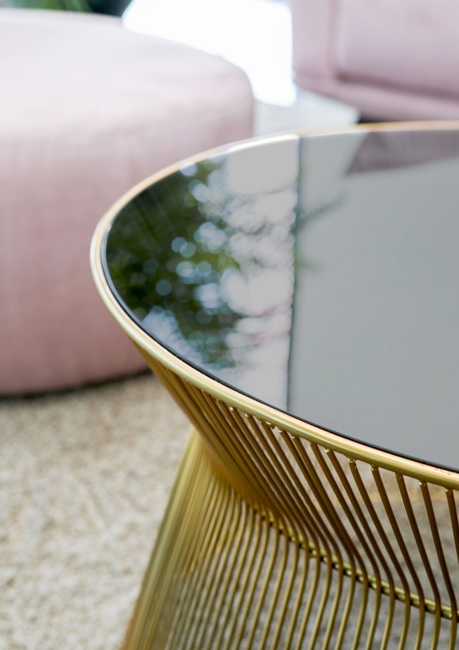 Close-up van een elegante salontafel met een zwart glazen blad en een goudkleurig metalen onderstel, gezien vanaf de zijkant.