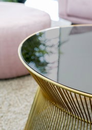 Nahaufnahme eines eleganten Couchtisches mit schwarzer Glasplatte und goldfarbenem Metallgestell, seitliche Perspektive.