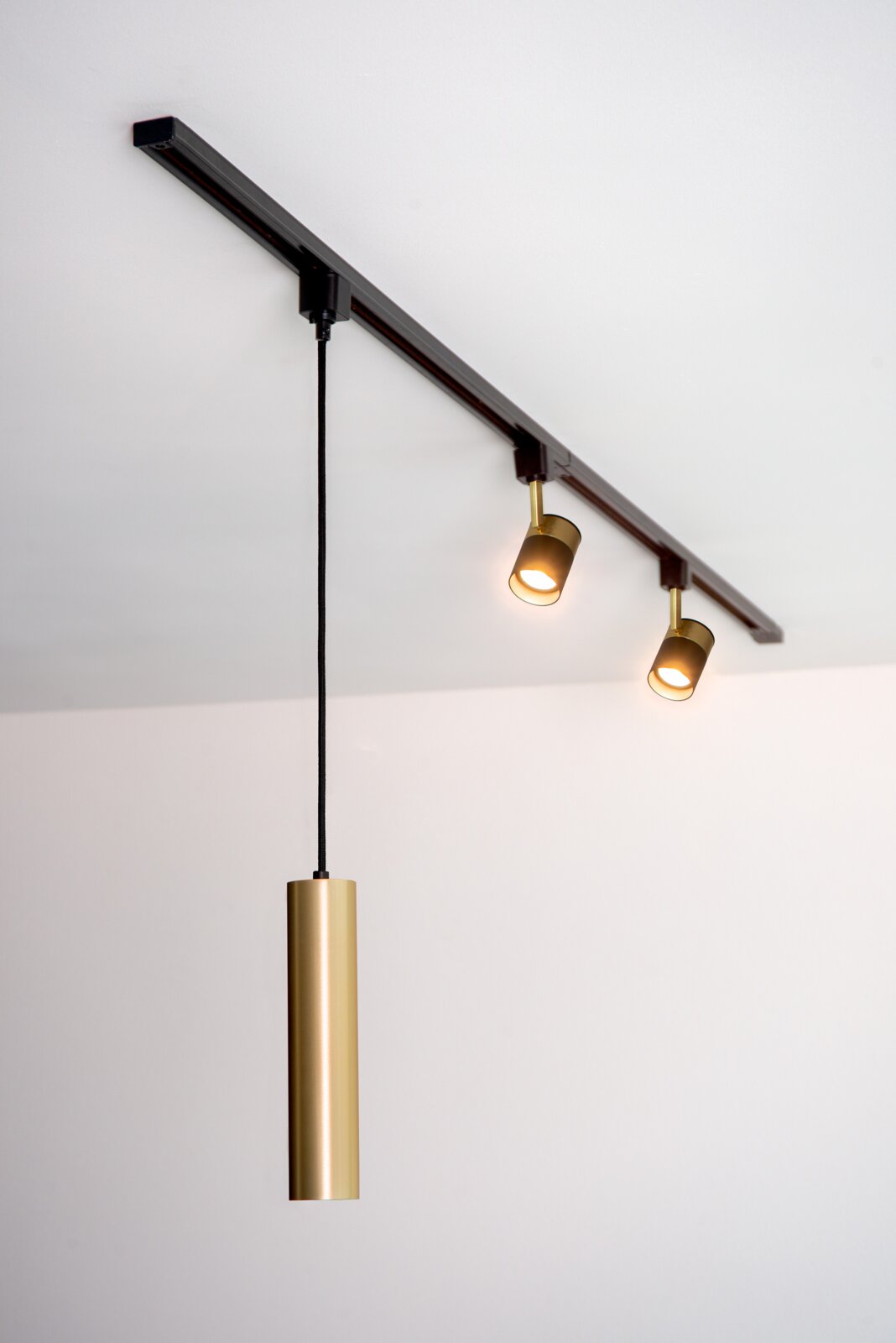 Deckenstrahler FLORIS in Schwarz mit zwei verstellbaren Leuchten und einem hängenden, zylindrischen Element in Gold, seitliche Perspektive.