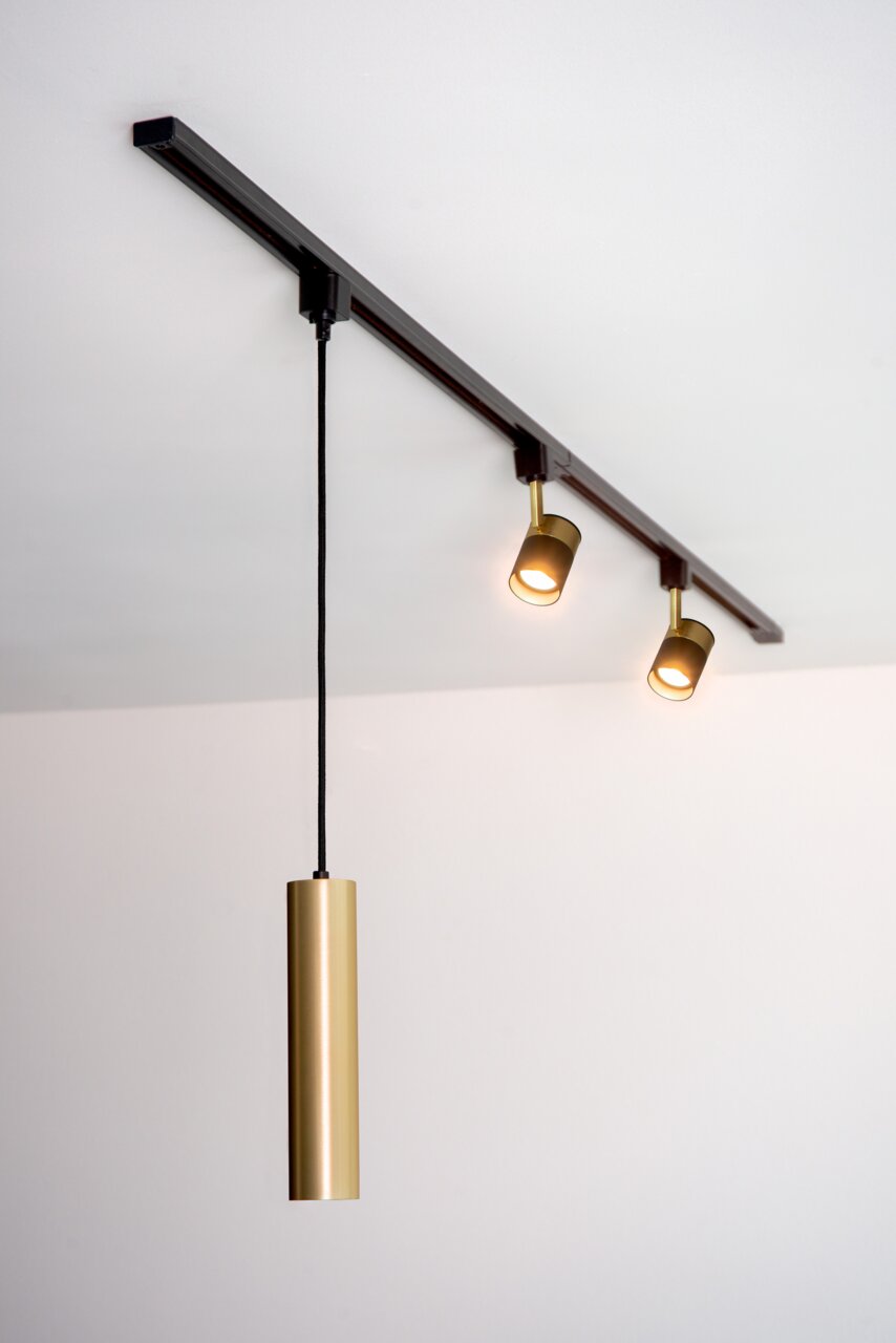 Deckenstrahler FLORIS in Schwarz mit zwei verstellbaren Leuchten und einem hängenden, zylindrischen Element in Gold, seitliche Perspektive.