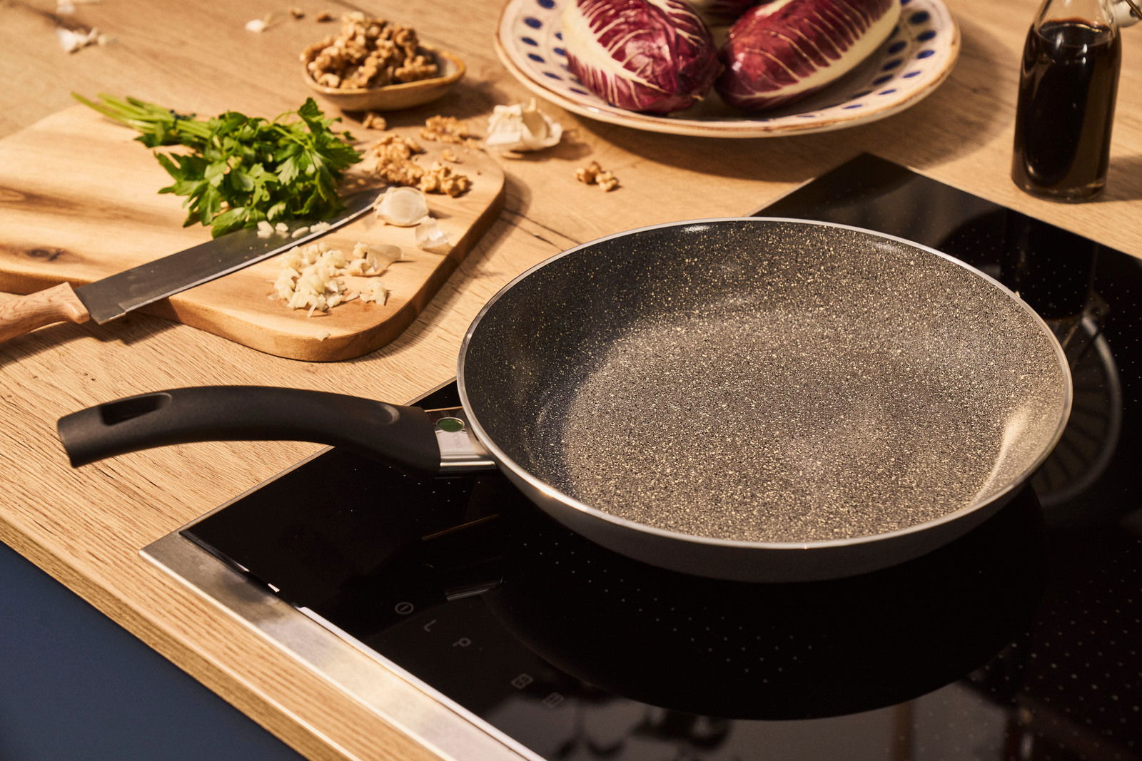 Bratpfanne mit 24 cm Durchmesser auf einem Herd, umgeben von frischen Zutaten auf einem Schneidebrett, aus der Vogelperspektive.