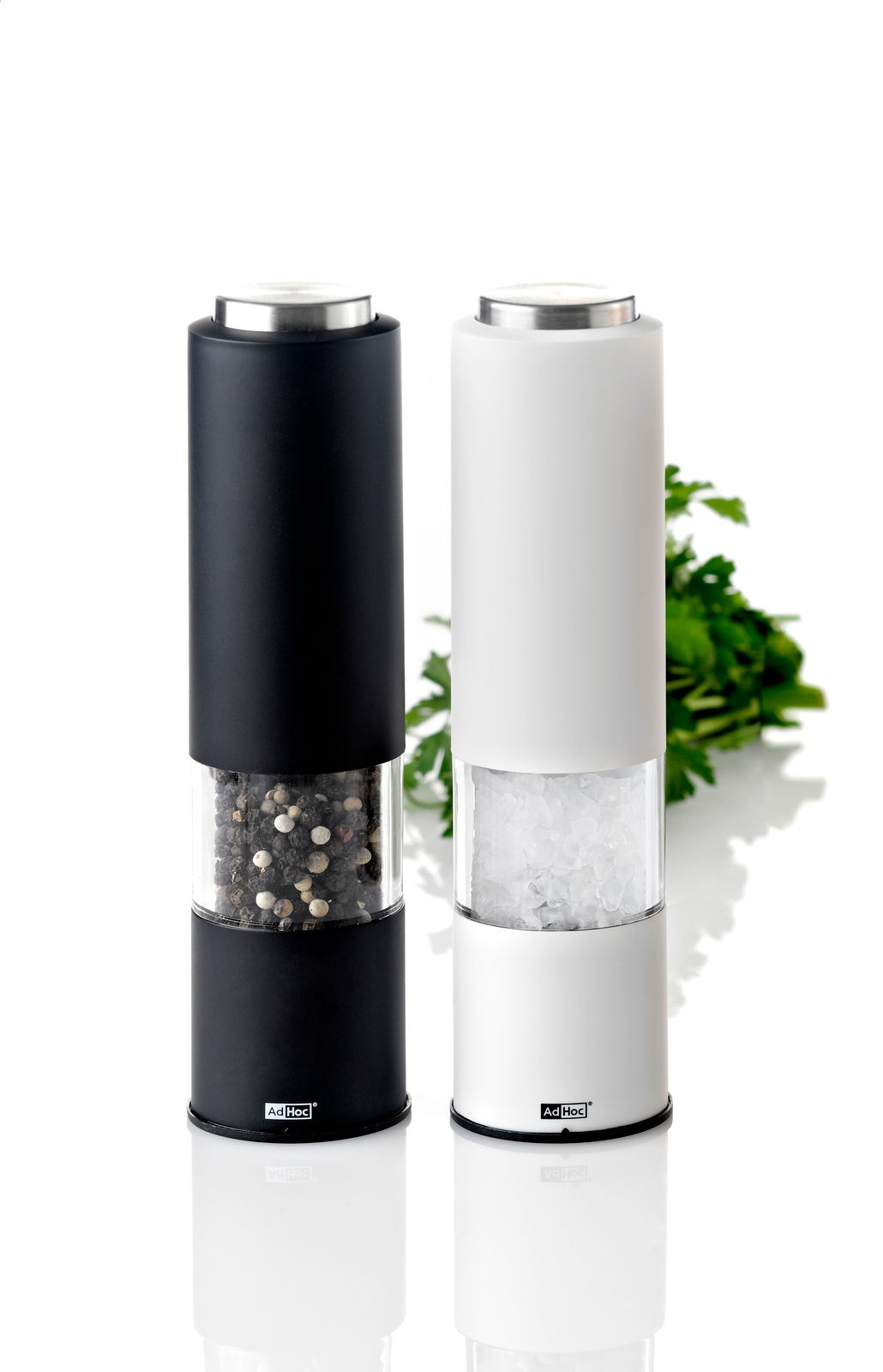 Zwei moderne Mühlen in Schwarz und Weiß, gefüllt mit Pfeffer und Salz, auf einer reflektierenden Oberfläche, frontal fotografiert.