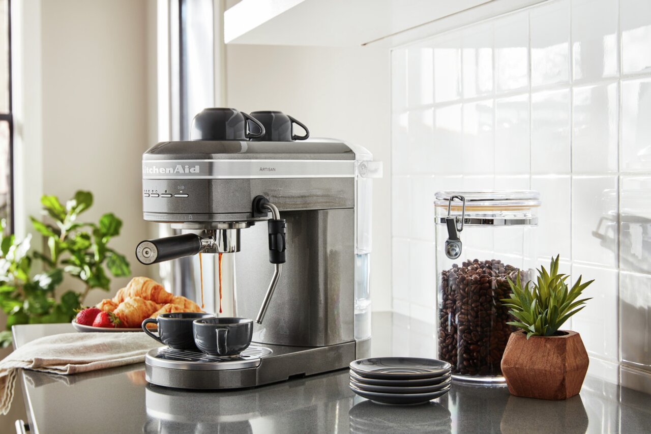 Edelstahl-Espressomaschine in einer modernen Küche, seitliche Perspektive, mit zwei Tassen und frischen Croissants.