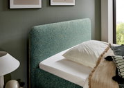 Seitliche Ansicht eines Polsterbetts mit grünem Kopfteil, dekoriert mit Kissen und Decken in einem modernen Schlafzimmer.