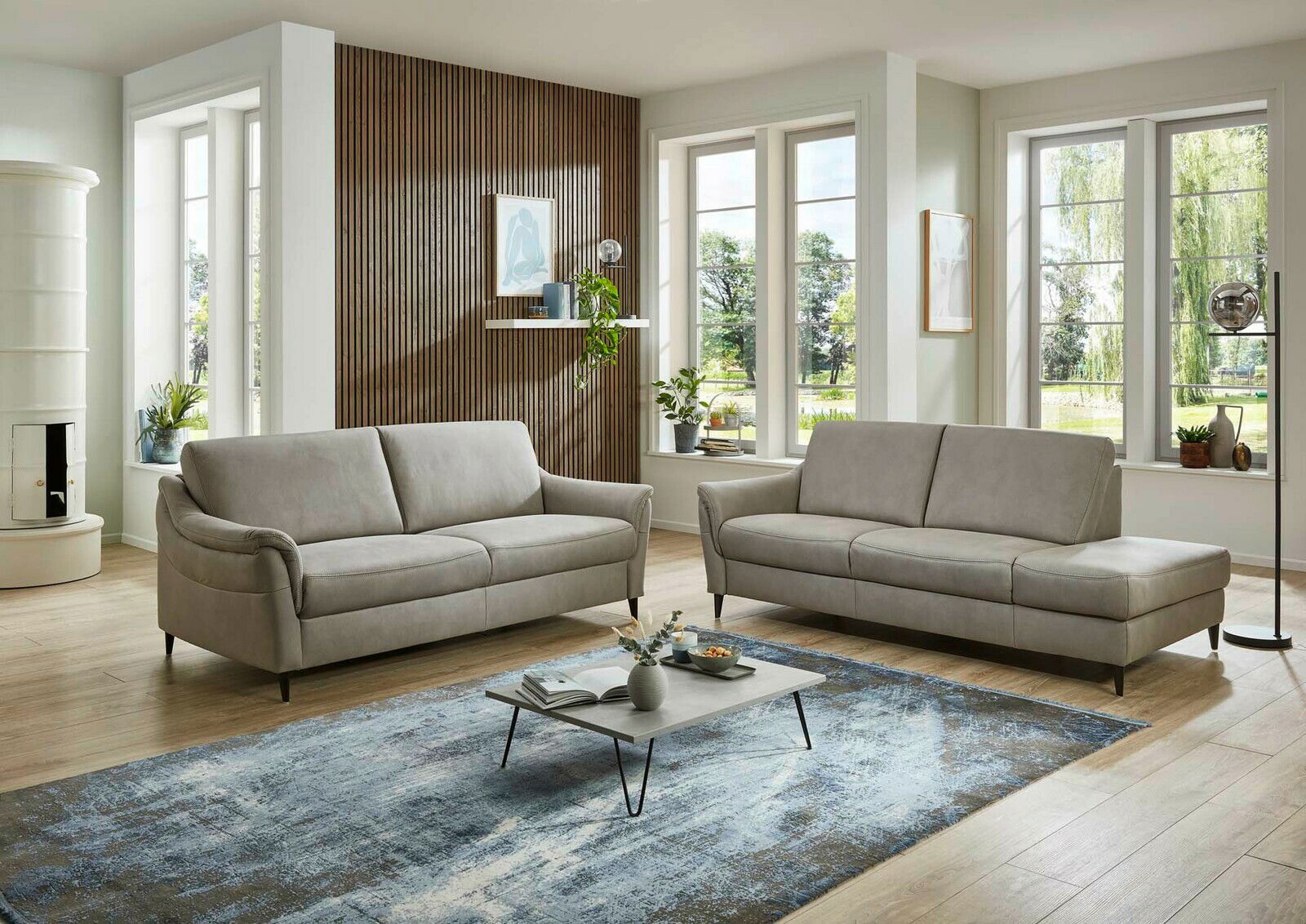 Moderne Wohnzimmeransicht mit zwei grauen Sofas, einem Couchtisch und großen Fenstern im Hintergrund. Perspektive von vorne.