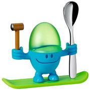 Blauer Eierbecher McEgg mit grünem Deckel, hält einen Löffel und einen kleinen Hammer, auf einem grünen Sockel stehend, Frontalansicht.