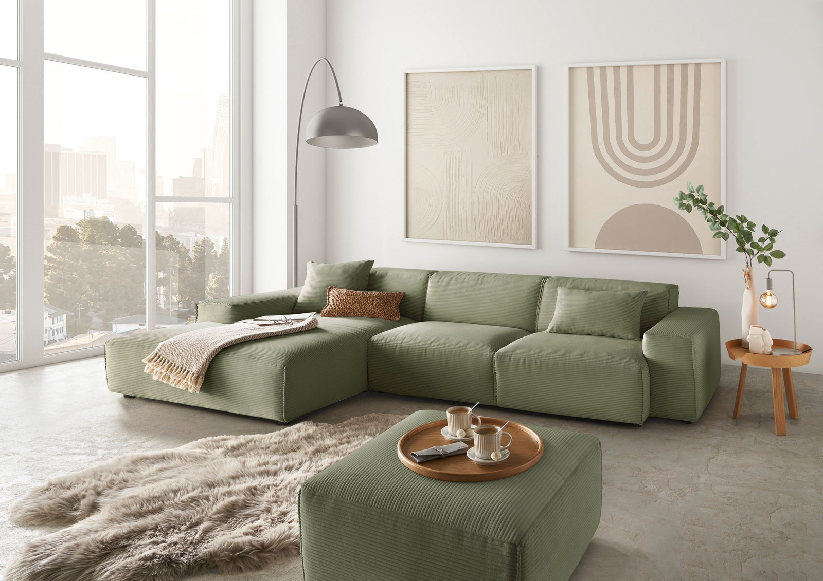 Grünes modulares Sofa in einem modernen Wohnzimmer mit großen Fenstern, zwei abstrakten Kunstwerken an der Wand und einem flauschigen Teppich, aus der Perspektive von vorne links.