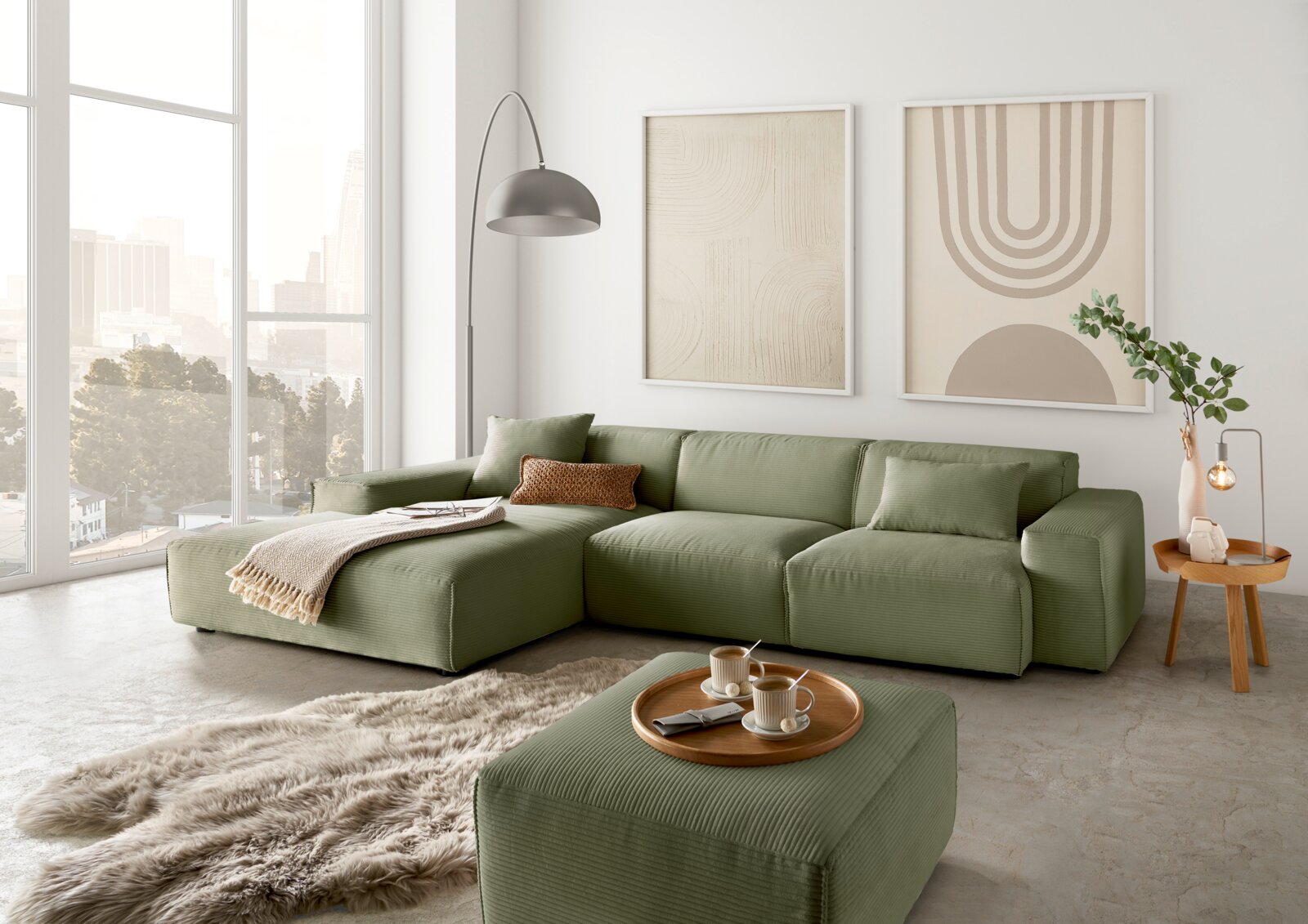 Lounge Handmade Ecksofa LH-EDINA Grünes modulares Sofa in einem modernen Wohnzimmer mit großen Fenstern, zwei abstrakten Kunstwerken an der Wand und einem flauschigen Teppich, aus der Perspektive von vorne links.