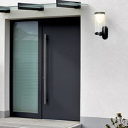 Moderne Akku-Außenwandleuchte an einer Hauswand neben einer Eingangstür, seitliche Perspektive