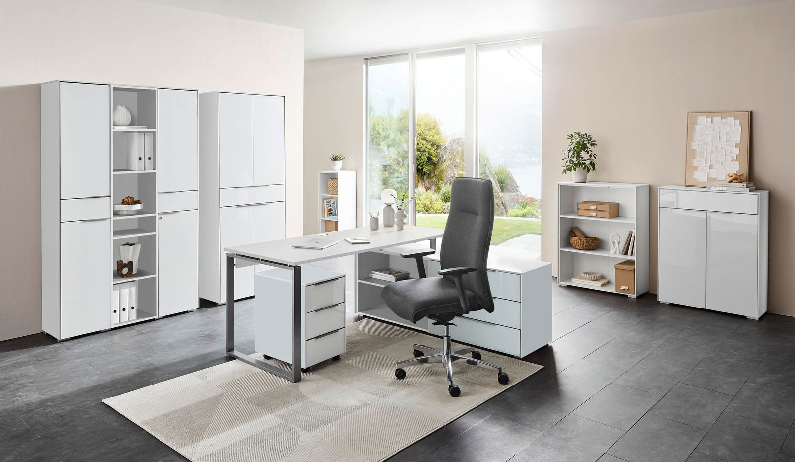 Voleo Aktenschrank NEVADA Moderne Büromöbelkombination mit Schreibtisch, Rollcontainer und Aktenschränken in einem hellen Raum mit Blick auf den Garten, aus der Perspektive von vorne.