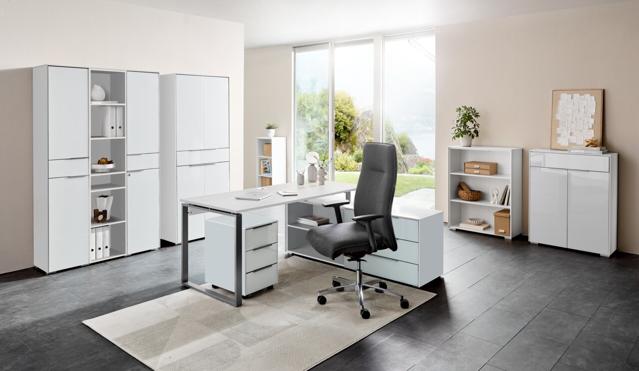 Voleo Aktenschrank NEVADA Moderne Büromöbelkombination mit Schreibtisch, Rollcontainer und Aktenschränken in einem hellen Raum mit Blick auf den Garten, aus der Perspektive von vorne.