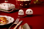 Weihnachtliches Salz- und Pfefferstreuer-Set aus weiß-rotem Porzellan mit Teddy-, Geschenk- und Spielzeugzugmotiven, in frontaler Dreiviertelansicht auf einer festlich gedeckten roten Tafel