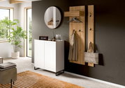 Modernes Garderoben-Set aus hellem Holz an dunkler Wand mit Hakenleiste und Kleiderbügeln, daneben weißer Schuhschrank auf Metallfüßen und runder Wandspiegel; Perspektive: frontale leicht seitliche Ansicht im Flur.