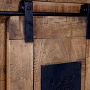 Close-up van een rustiek houten secretaire met een zwart metalen schuifmechanisme en een metalen plaatje met het opschrift '1867'.
