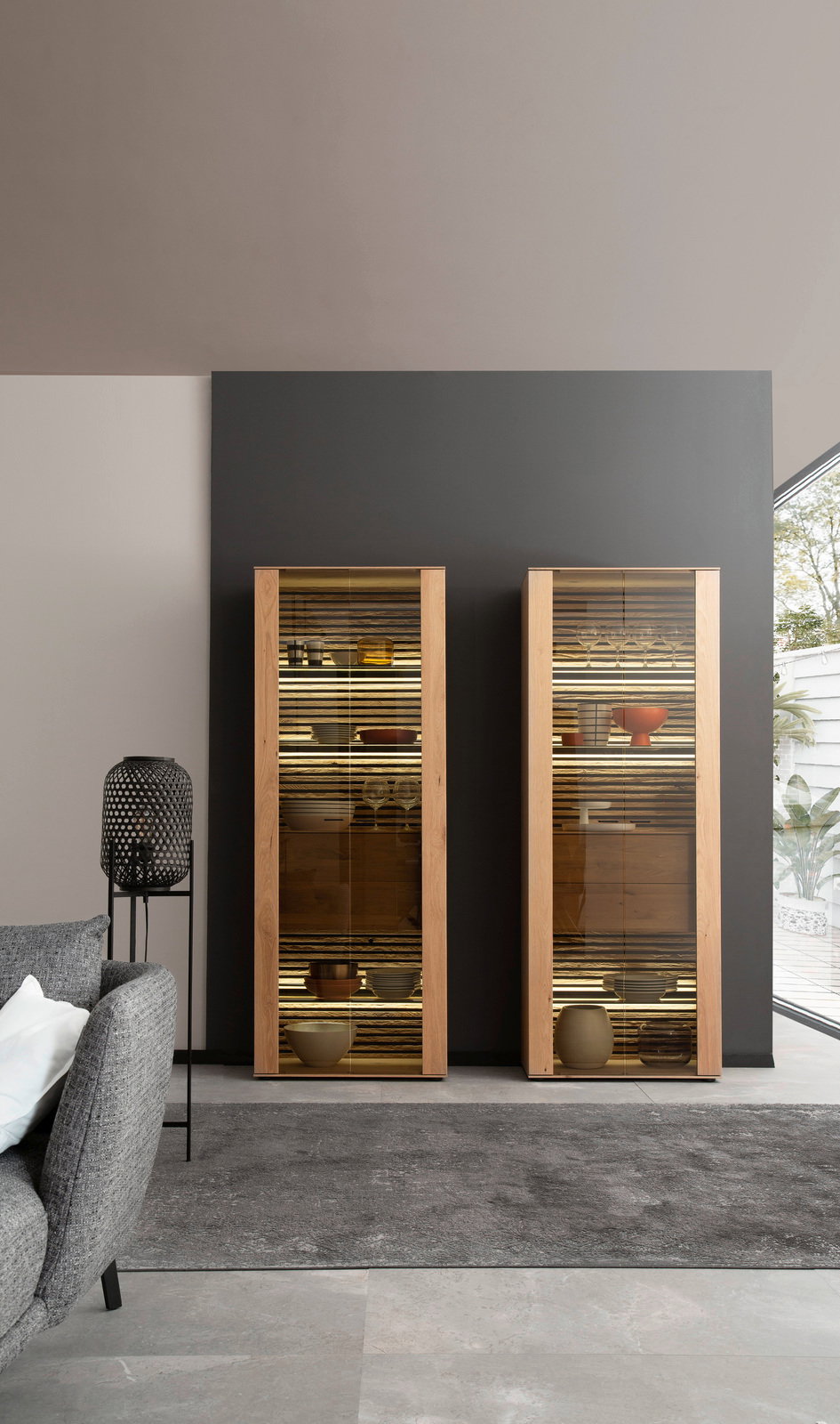 Zwei moderne Vitrinen mit Holzrahmen und Glastüren, frontal fotografiert, gefüllt mit Geschirr und dekorativen Objekten, in einem stilvollen Wohnzimmer.