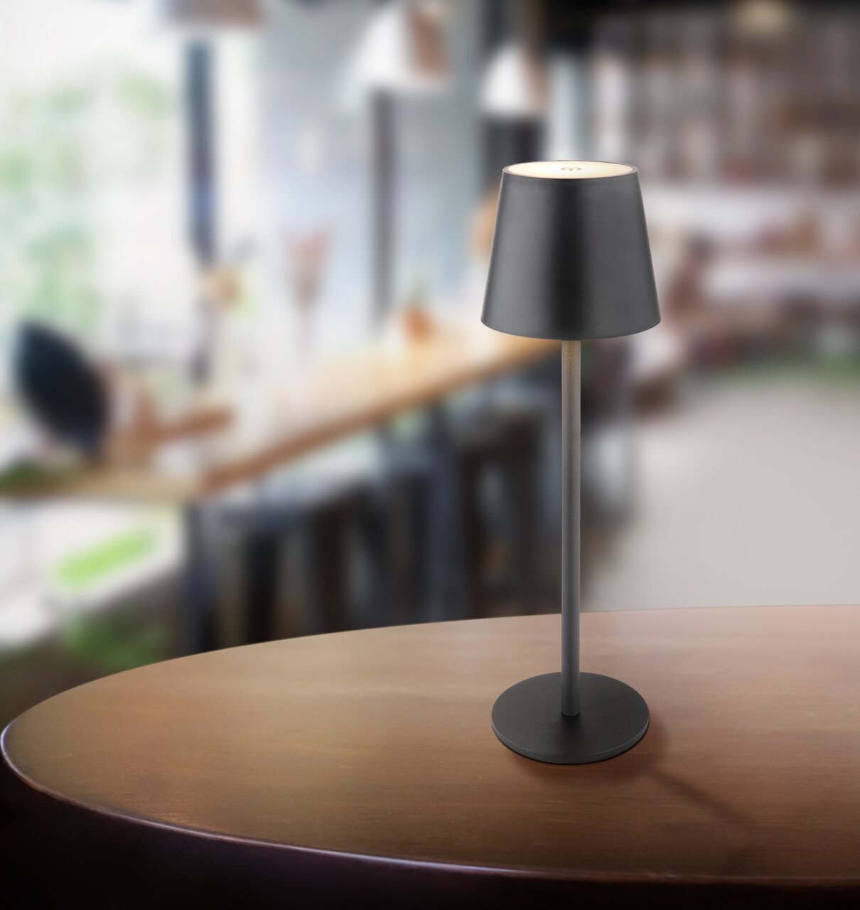 Moderne Akku-Tischleuchte VANNIE in einem stilvollen Café, seitliche Perspektive