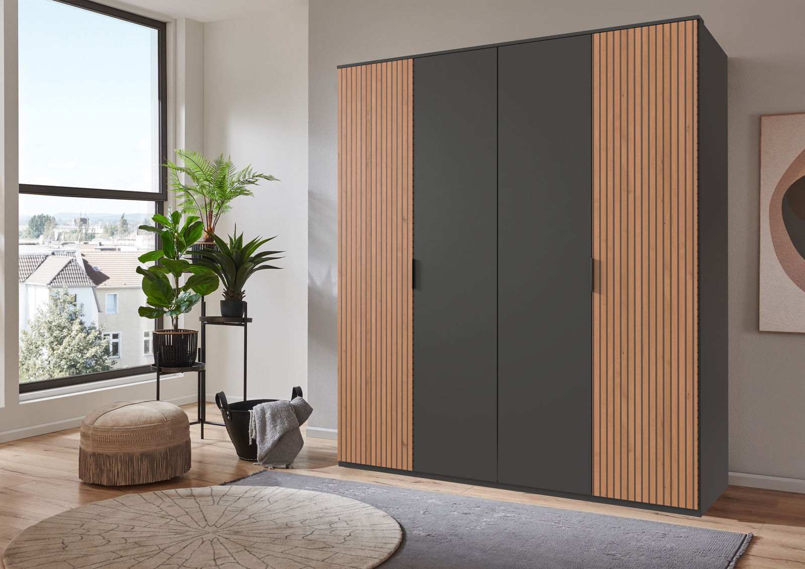 Moderner Drehtürenschrank mit vier Türen, in einer stilvollen Kombination aus dunklem Grau und Holzoptik, in einem hellen Raum mit Pflanzen und einem großen Fenster, seitliche Perspektive.
