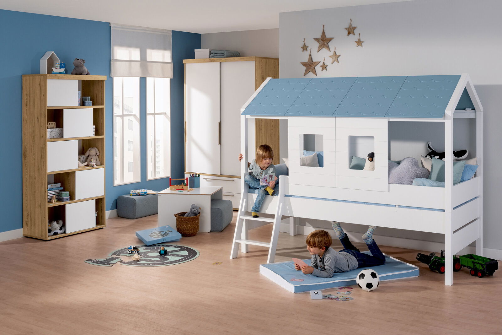 Paidi Dachschindel TINY-HOUSE Kinderzimmer mit einem Hochbett in Form eines Hauses mit blauen Dachschindeln, zwei spielende Kinder, eines auf der Leiter und eines auf einer Matte darunter, Perspektive von vorne.