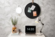 Rundes schwarzes Memoboard an der Wand mit drei befestigten Karten, umgeben von einem dekorativen Spiegel, einer Tischlampe und einem Laptop auf einem Schreibtisch. Perspektive: Frontalansicht.