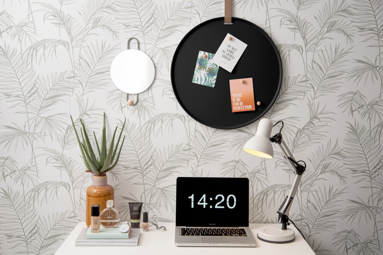 Rundes schwarzes Memoboard an der Wand mit drei befestigten Karten, umgeben von einem dekorativen Spiegel, einer Tischlampe und einem Laptop auf einem Schreibtisch. Perspektive: Frontalansicht.